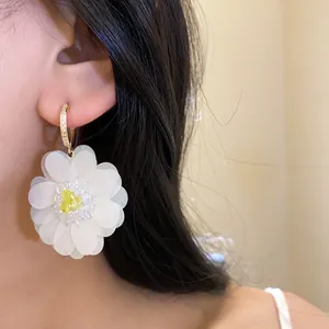 Elegant close-up of large white organza flower earrings with a gold hoop on a model's ear