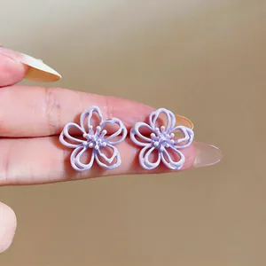 Detailaufnahme der violetten hohlen Blumenohrringe zur Größenreferenz an den Fingern