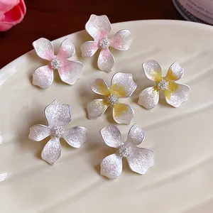 Close-up view of delicate enamel flower stud earrings in pink, yellow and white colors