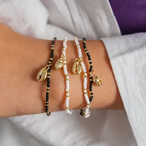 Macro view of bohemian beaded bracelets featuring gold sea shell charms on a wrist