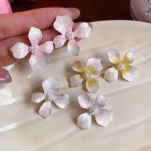 Close-up detail of enamel flower stud earrings with delicate pink and yellow color gradients