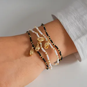 Detail of layered seed bead bracelets with golden conch shell charms on wrist.