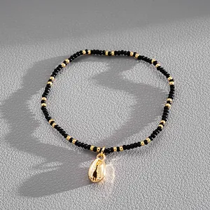 Macro detail of golden cowrie shell charm on black and gold seed bead vacation bracelet