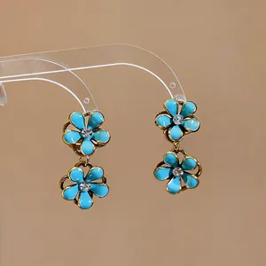 Close-up of blue enamel flower drop earrings with rhinestones on a clear display stand