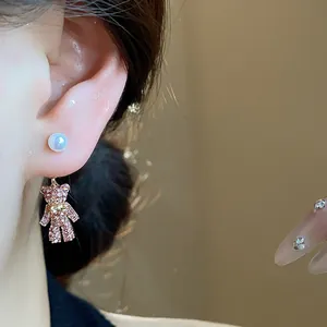 Detailaufnahme eines funkelnden rosa Bärenohrrings mit Perlenstecker direkt am Ohr