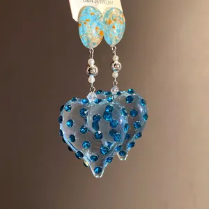Detailed macro view of vintage blue resin heart earrings with rhinestones and pearls.