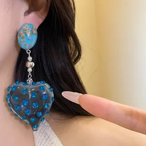 Close-up detail of vintage resin heart drop earring with blue rhinestones worn on ear