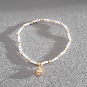 Detailed view of a white seed bead bracelet with a polished golden conch shell charm.