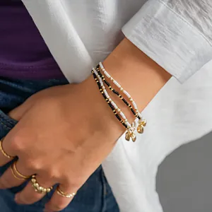 Close-up of a three-piece seed bead bracelet set with golden heart charms on a wrist