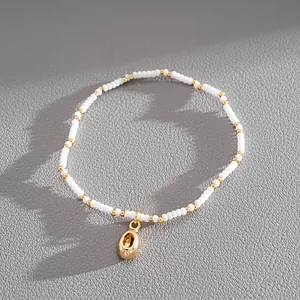 Detail view of white seed bead bracelet with a gold shell pendant on grey texture.