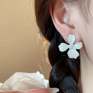 Close-up view of elegant white flower earring with fine sparkling texture on model's ear.
