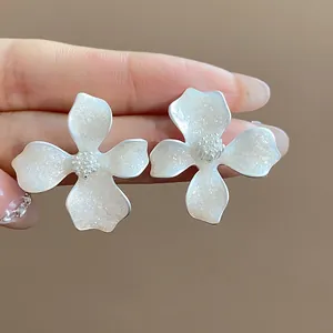 Detailed close-up of elegant white enamel flower stud earrings with shimmering texture
