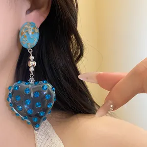 Close-up detail of vintage heart resin earrings featuring blue rhinestones and gold flakes