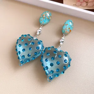 Close-up of vintage resin heart earrings with sparkling blue rhinestones and gold foil detail.