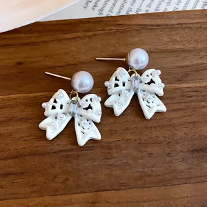 Primo piano di orecchini a perno con fiocco bianco traforato, piccole perle e cristallo.