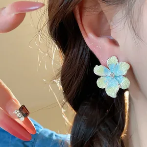 Détail d'une boucle d'oreille fleur en zircon coloré et d'une bague élégante portée