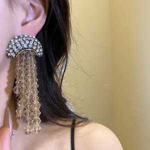 Close-up of champagne crystal tassel earrings with sparkling rhinestone studs worn on ear.