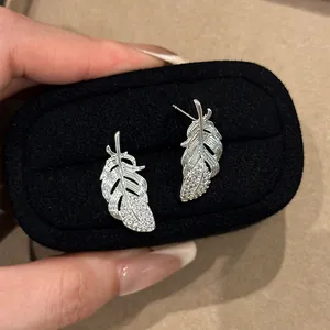 Detailed close-up of silver feather stud earrings with sparkling rhinestones in a box.
