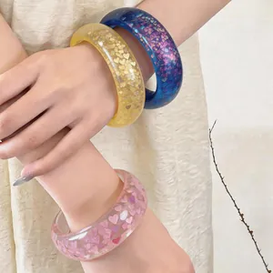 Close-up of vibrant resin bangles featuring heart-shaped glitters on model arms.