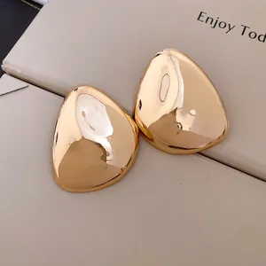 Detail von übergroßen, polierten goldenen geometrischen Ohrsteckern im minimalistischen Look