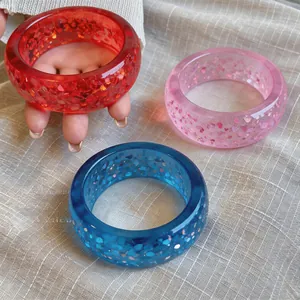Close-up of three vibrant resin bangles with embedded glitter in red, pink, and blue