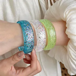 Detail shot of three colorful shimmering dopamine resin bangles worn on a wrist with ruffled sleeve