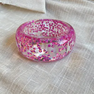 Close-up of a chunky transparent resin bangle with embedded pink iridescent glitter.