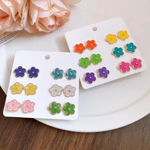 Dettaglio di 12 paia di orecchini colorati a forma di fiore su cartoncini bianchi.