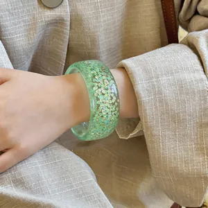 Detailed view of a light green resin bangle with iridescent heart glitter flakes.