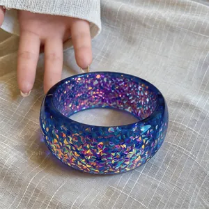 Close-up of a blue resin bangle with iridescent glitter embedded inside on linen cloth