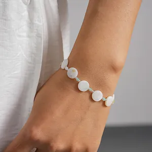 Close-up detail of a minimalist shell and glass bead circular geometric bracelet on wrist