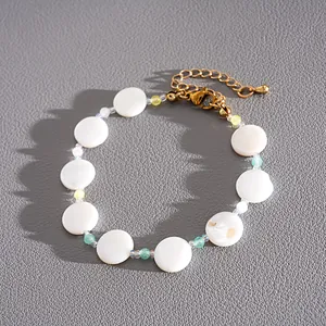 Close-up of minimalist white shell and glass bead bracelet on textured grey surface
