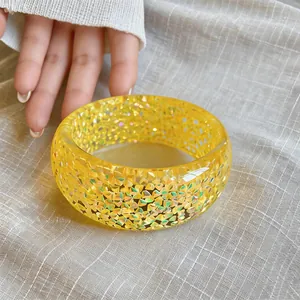 Detail shot of a vibrant yellow resin bangle with shimmering holographic glitter inside.