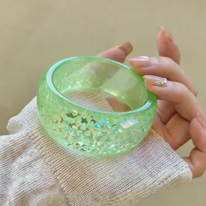 Macro detail of light green resin bangle with iridescent geometric flakes inside