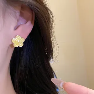 Primo piano di un orecchino a perno a forma di fiore giallo smaltato indossato sull'orecchio