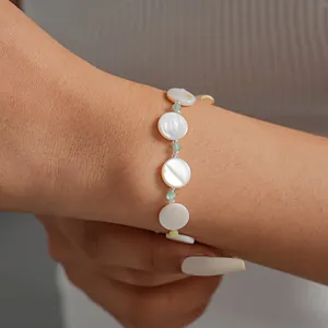 Close-up detail of a minimalist geometric shell and glass beaded bracelet on a woman's wrist
