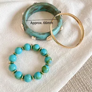 Dettaglio di set di braccialetti in resina con conchiglie e perline su tessuto testurizzato.