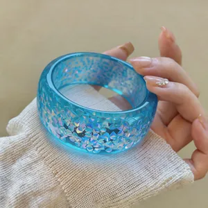 Close-up of a blue translucent resin bangle with iridescent shimmer on a person's wrist.