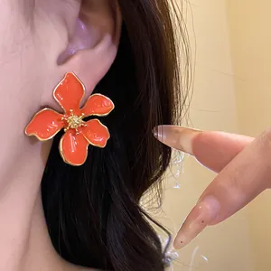 Close-up of bright orange flower drip oil earrings on model ear
