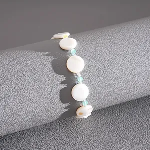 Detail showing circular shell pieces and green glass beads on a textured grey stand
