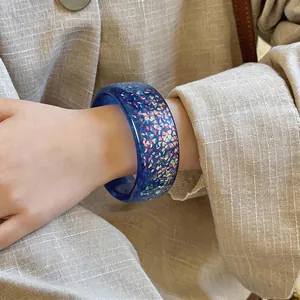 Close-up view of a blue resin bangle with iridescent glitter on a person's wrist.