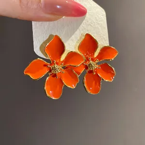 Detailed macro view of bright orange enamel flower stud earrings with elegant golden edges