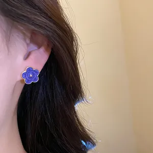 Primo piano di un orecchino a lobo a forma di fiore in smalto viola indossato da una modella