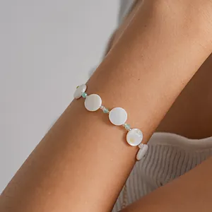 Close-up of elegant bracelet featuring round white shell discs and small green beads