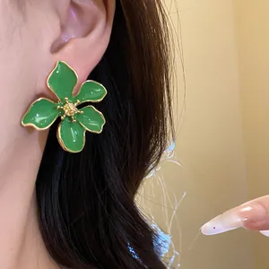 Detail of a green enamel flower stud earring worn on the ear with a gold-plated trim.