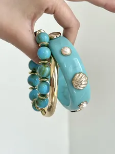 Dettaglio di bracciali in resina turchese con ciondoli a conchiglia dorati e perle