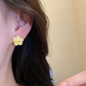 Primo piano di un dolce orecchino a lobo a fiore in smalto giallo su una modella.
