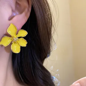 Close-up detail of a large vibrant yellow enamel flower stud earring worn on model
