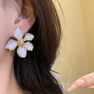 Close-up of elegant white enamel flower earring with gold trim on model.