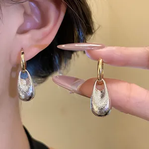 Detailed close-up of textured silver waterdrop pendant earrings with golden hoops on ear
